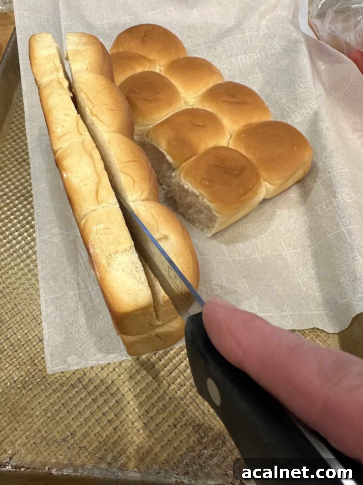 A knife slices dinner rolls in half.