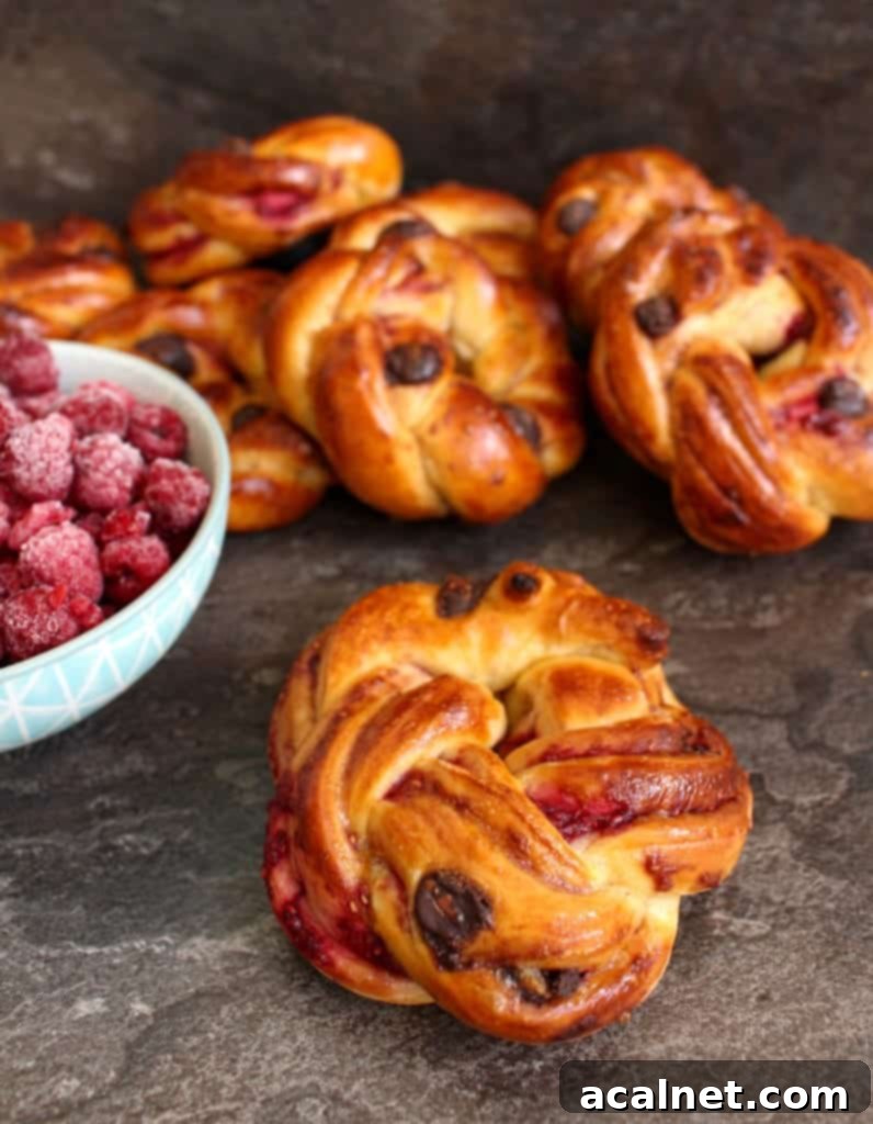 A perfectly baked brioche roll on a grey surface, with a blue bowl overflowing with fresh raspberries, hinting at the delightful filling.