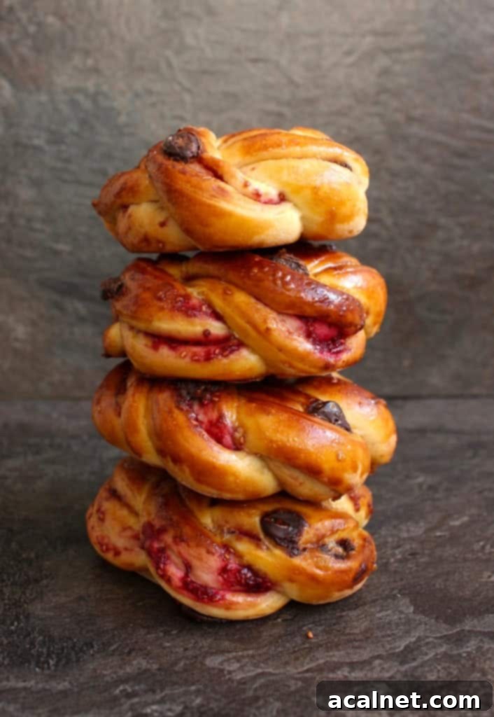 A tempting stack of freshly baked Raspberry and Chocolate Chip Brioche Buns, showcasing their golden crusts and intricate swirls.