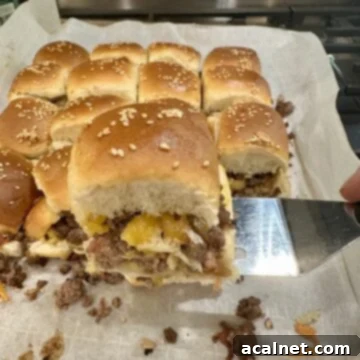A spatula serving a perfectly golden-brown cheeseburger slider from a baking pan on the stovetop, highlighting melted cheese.