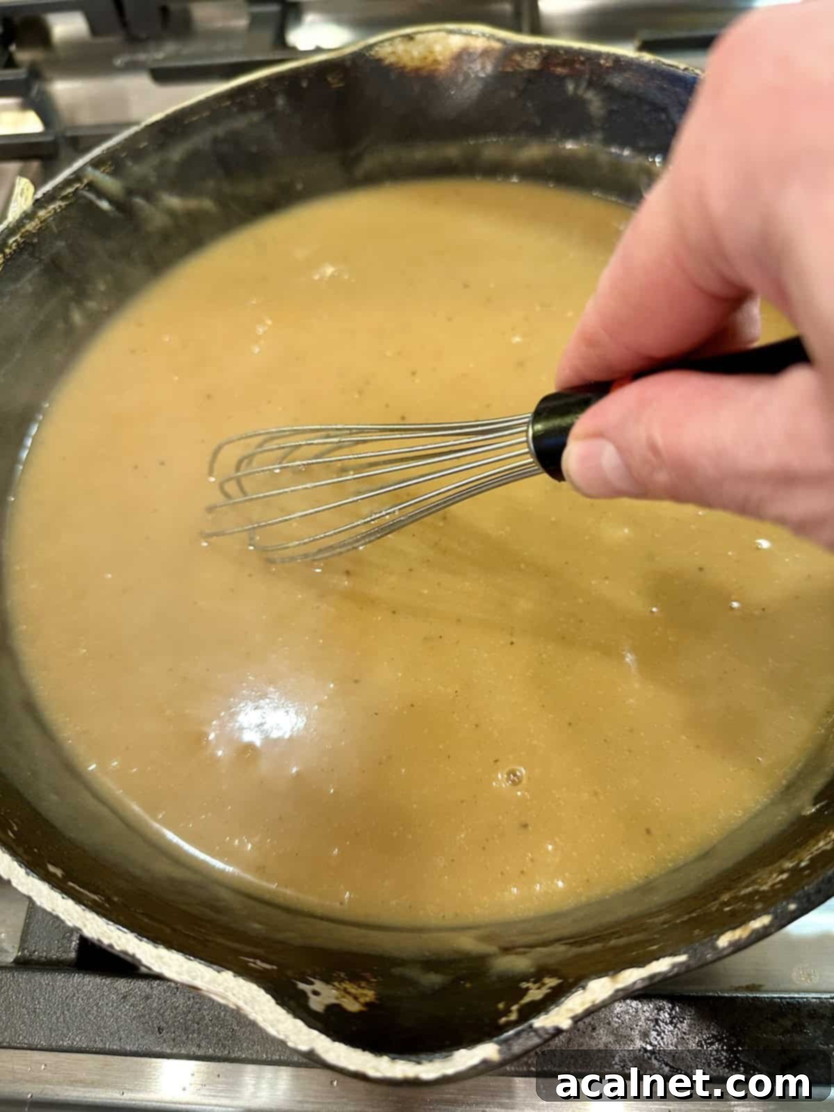 A skillet full of finished, thick gravy with a whisk resting inside.