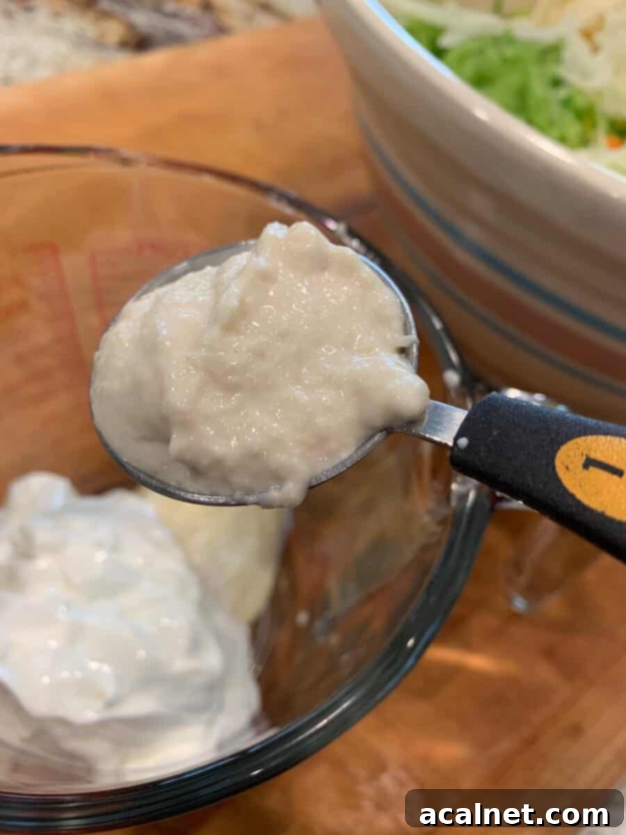 A spoonful of horseradish sauce next to other cole slaw dressing ingredients, emphasizing its role in the unique flavor profile.