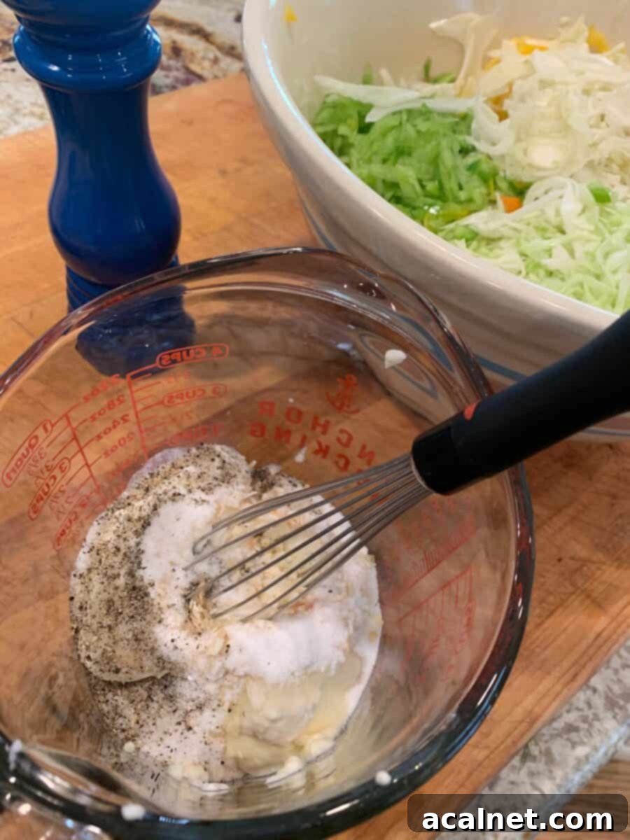 Cole slaw dressing ingredients being whisked together in a glass measuring cup, showing the smooth, creamy consistency forming.
