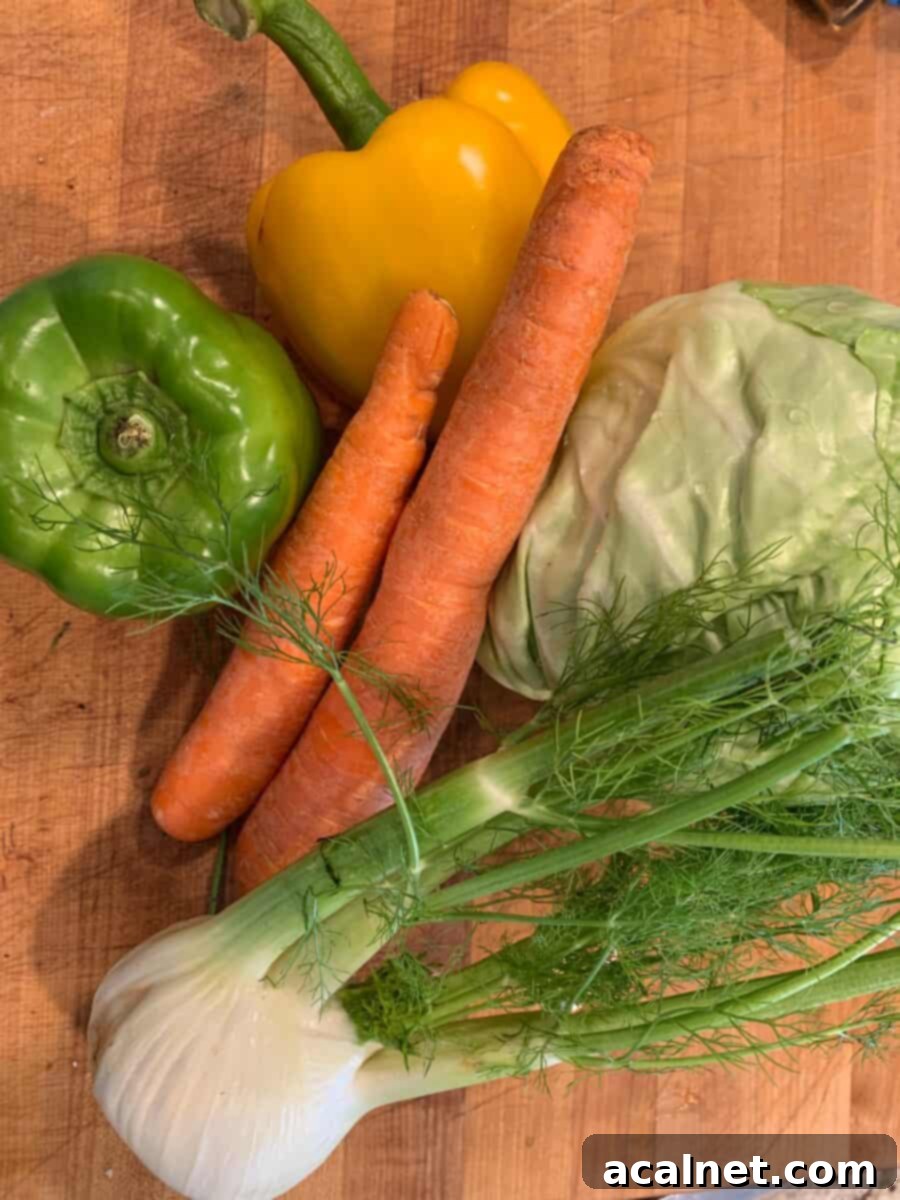 Fresh cole slaw ingredients including cabbage, green and yellow bell peppers, carrots, and a fennel bulb neatly arranged on a wooden cutting board, ready for preparation.