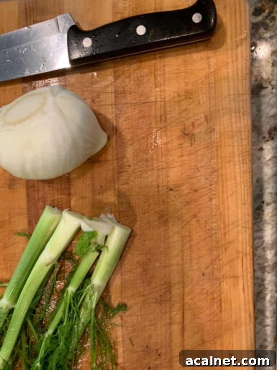 A fennel bulb neatly cut in half on a wooden cutting board, revealing its layered, crisp interior structure.