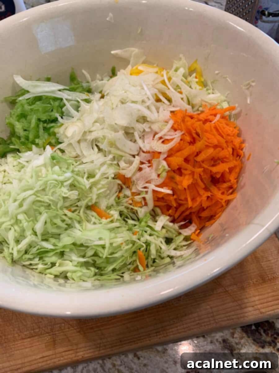 A large bowl filled with freshly shredded cole slaw ingredients, including cabbage, carrots, and peppers, ready for the dressing.