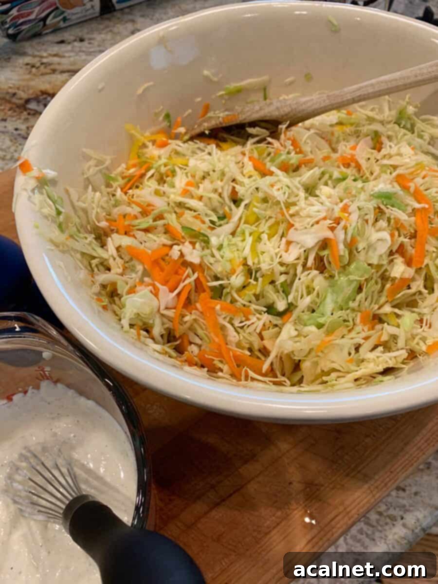 Shredded cole slaw ingredients and grated carrots in a bowl, with a separate small bowl of creamy dressing on the side.