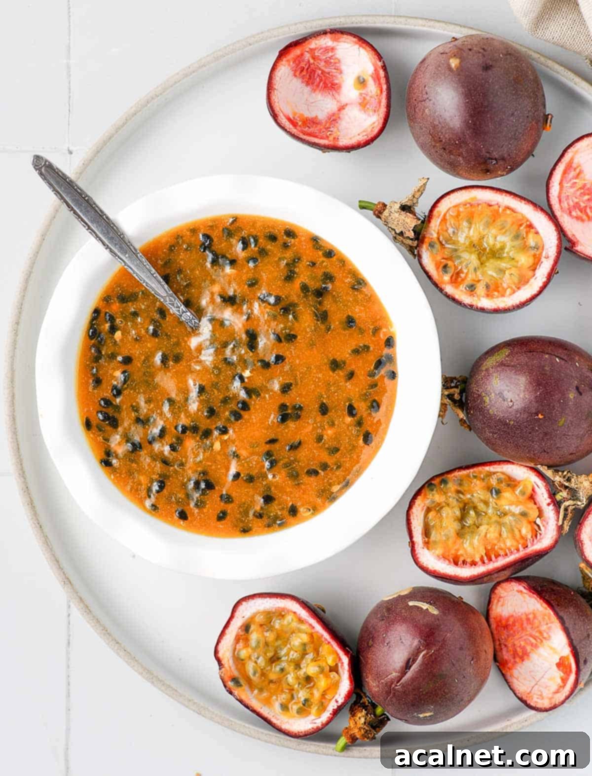Effortless Passion Fruit Coulis 11 Coulis in a white bowl over a large plate with fresh passion fruits, seen from above, ready to serve.