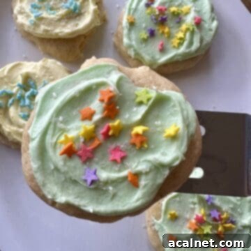 A frosted sour cream cookie on a spatula over a plate of cookies.