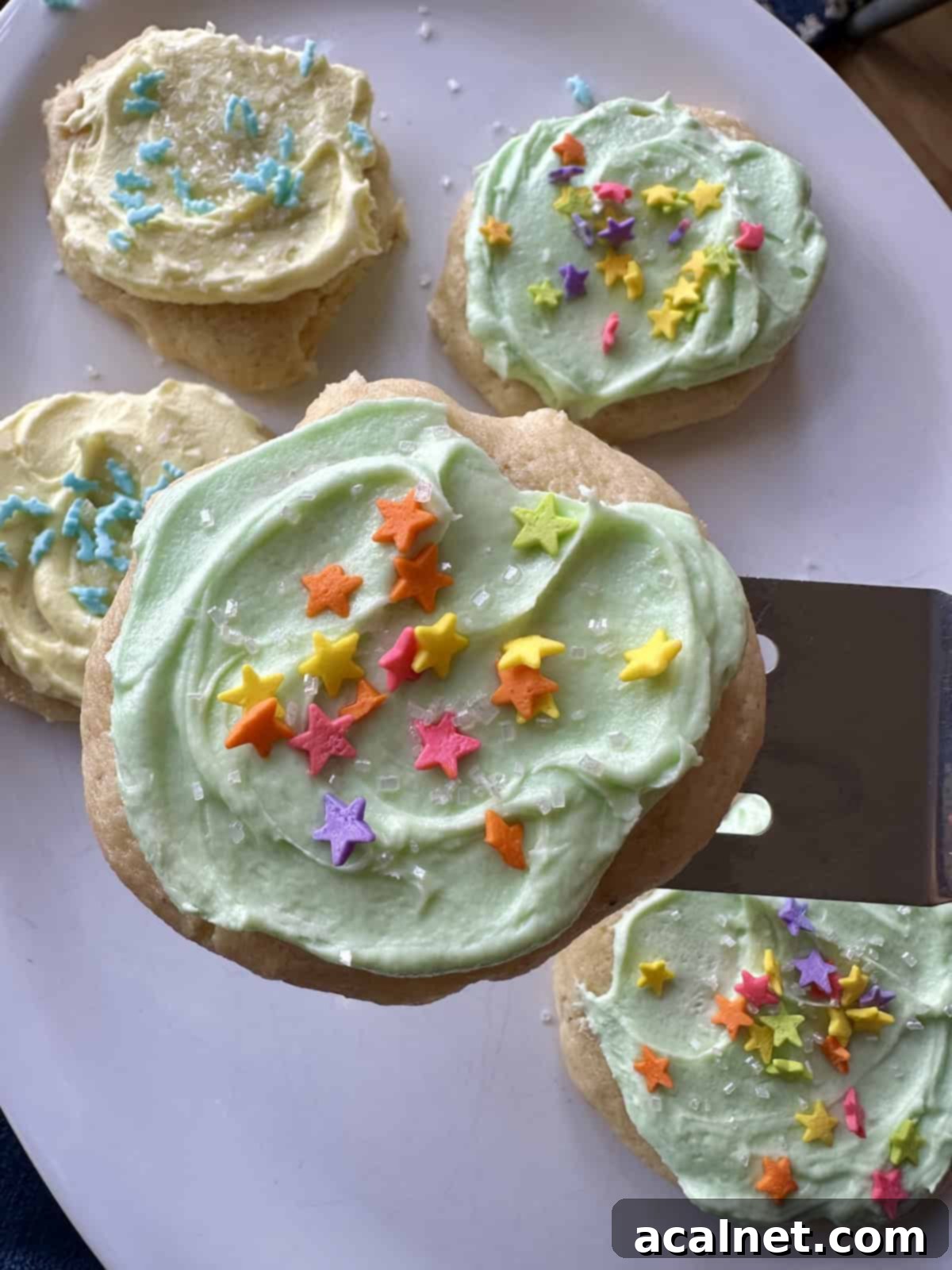 A frosted sour cream cookie on a spatula over a plate of cookies.