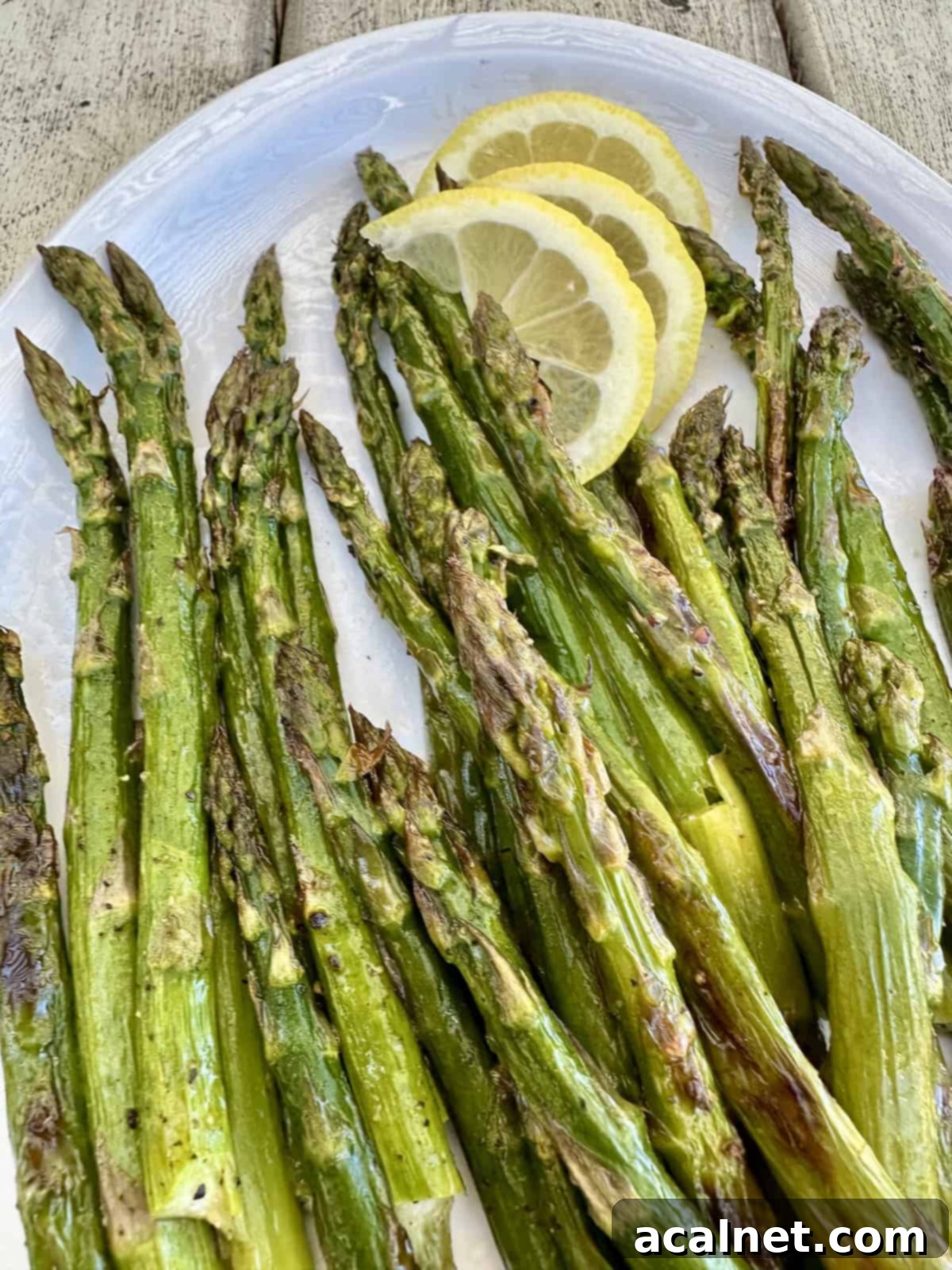 Vibrantly green pan-roasted asparagus spears arranged on a white plate, garnished with fresh lemon slices, highlighting their tender texture and the bright, citrusy accompaniment. A perfect healthy side dish.