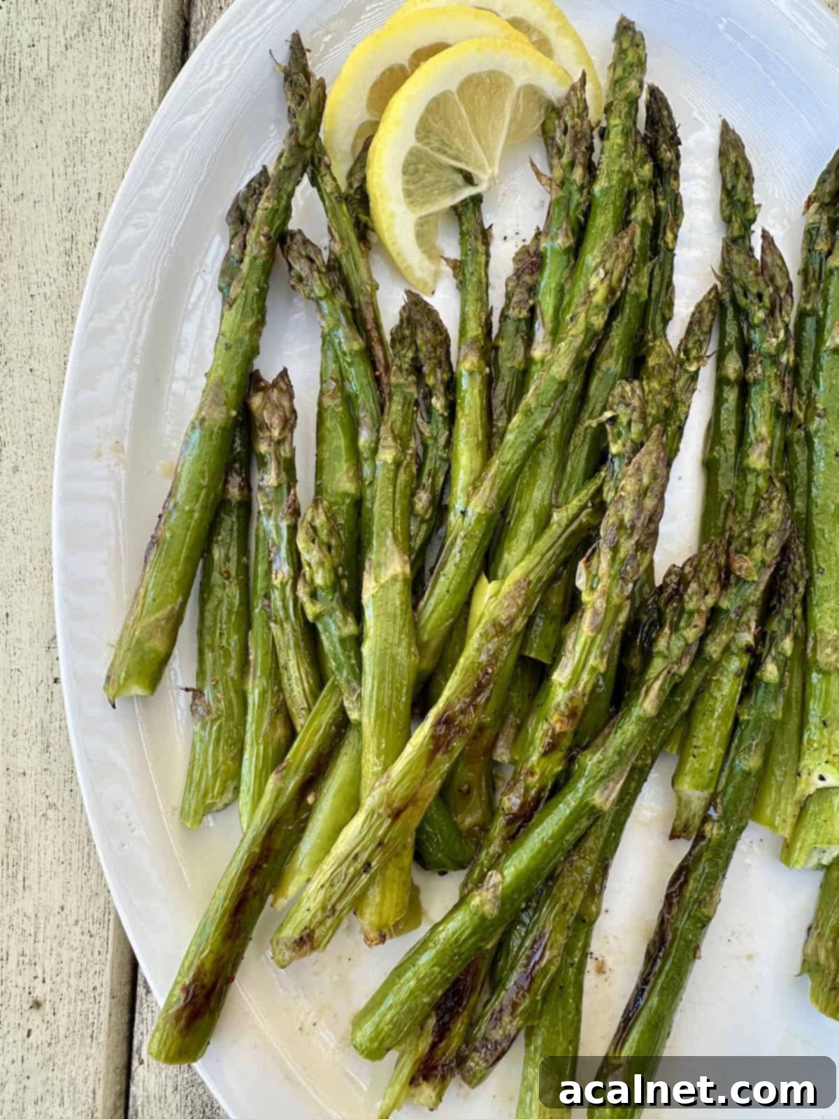 Close-up of perfectly pan-roasted asparagus on a white serving platter, garnished with fresh lemon wedges, emphasizing its golden-brown caramelization and vibrant green color.