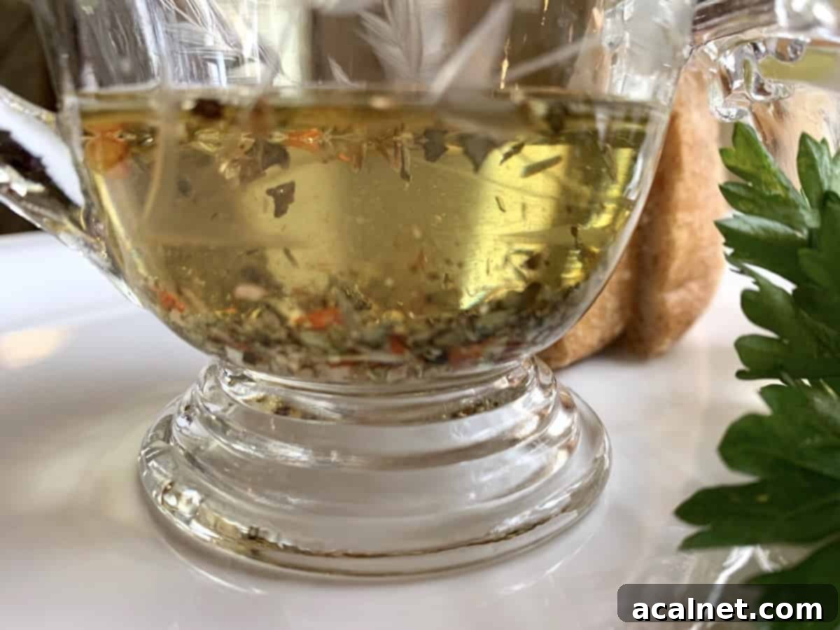 A small serving pitcher of olive oil with herbs, next to a bowl of bread