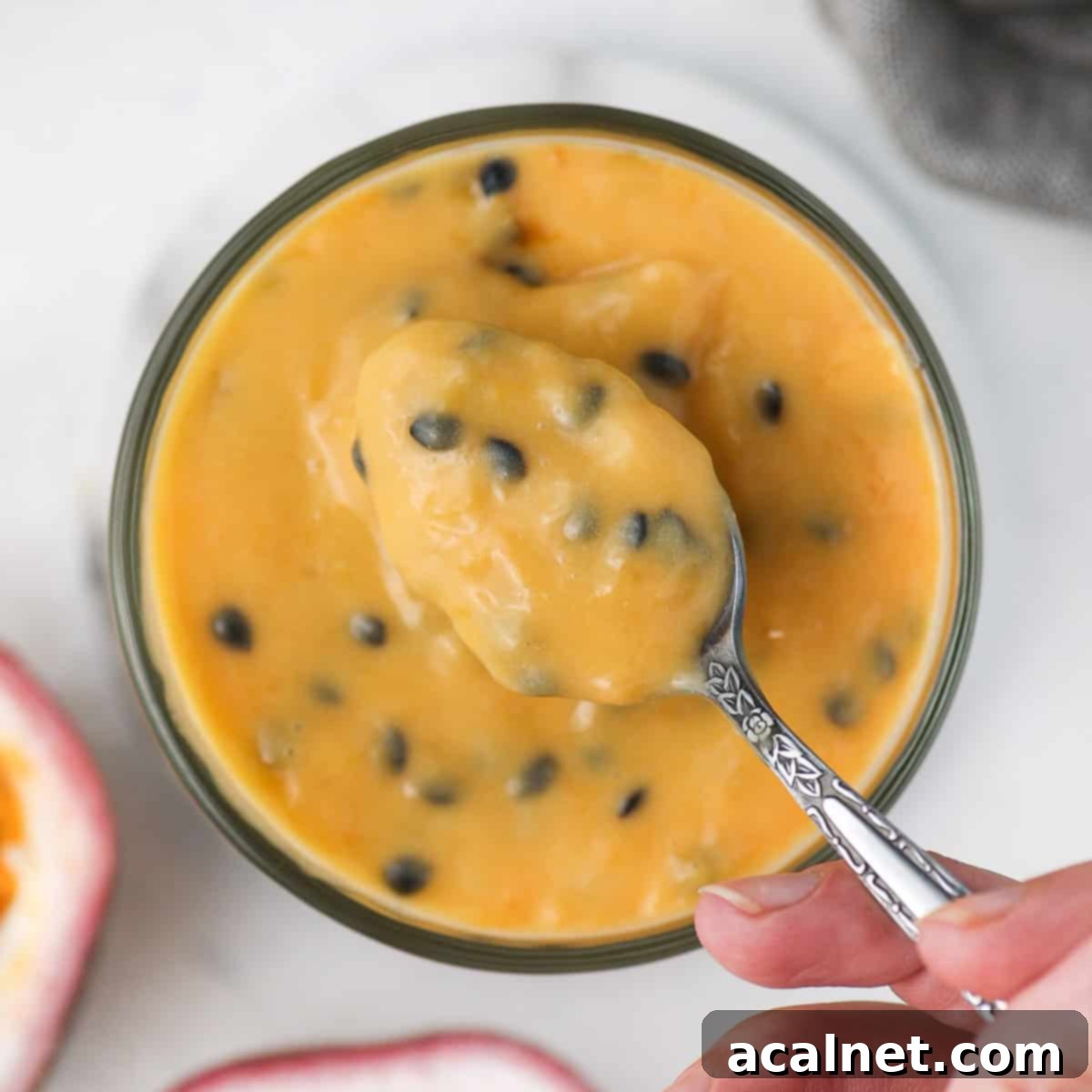 Picking up some vibrant passion fruit curd from a jar with a spoon, showcasing its rich yellow color and delightful seeds.