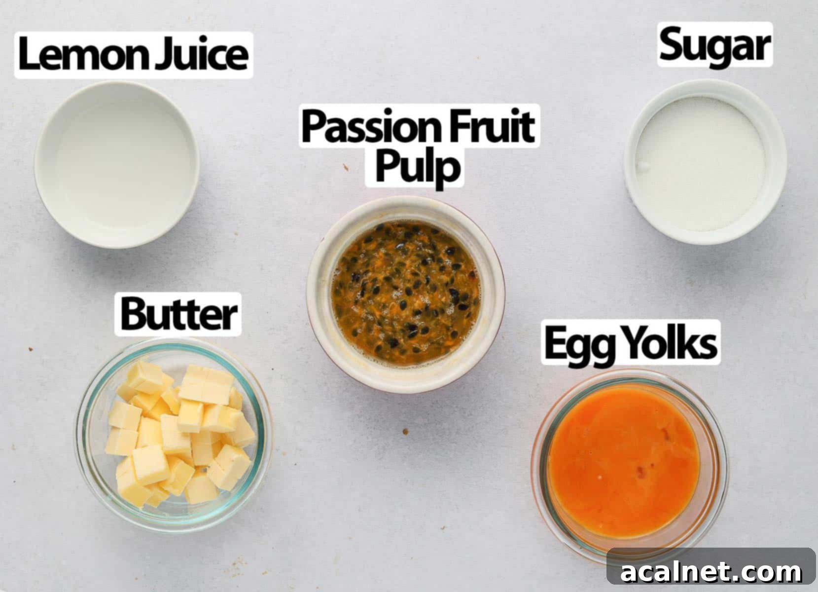 A flat lay of the 5 essential ingredients for passion fruit curd: fresh passion fruit, sugar, lemon, eggs, and butter, on a white surface.