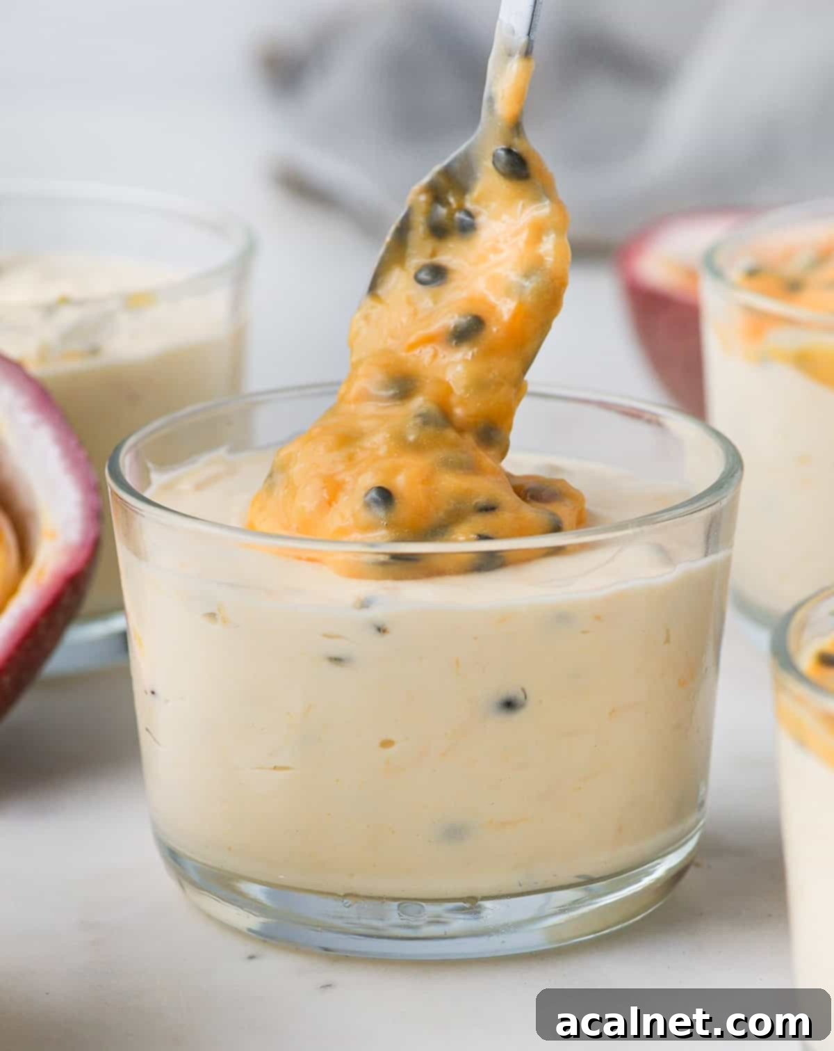 Pouring some glistening passion fruit curd over a glass cup of creamy passion fruit mousse, ready to be enjoyed.