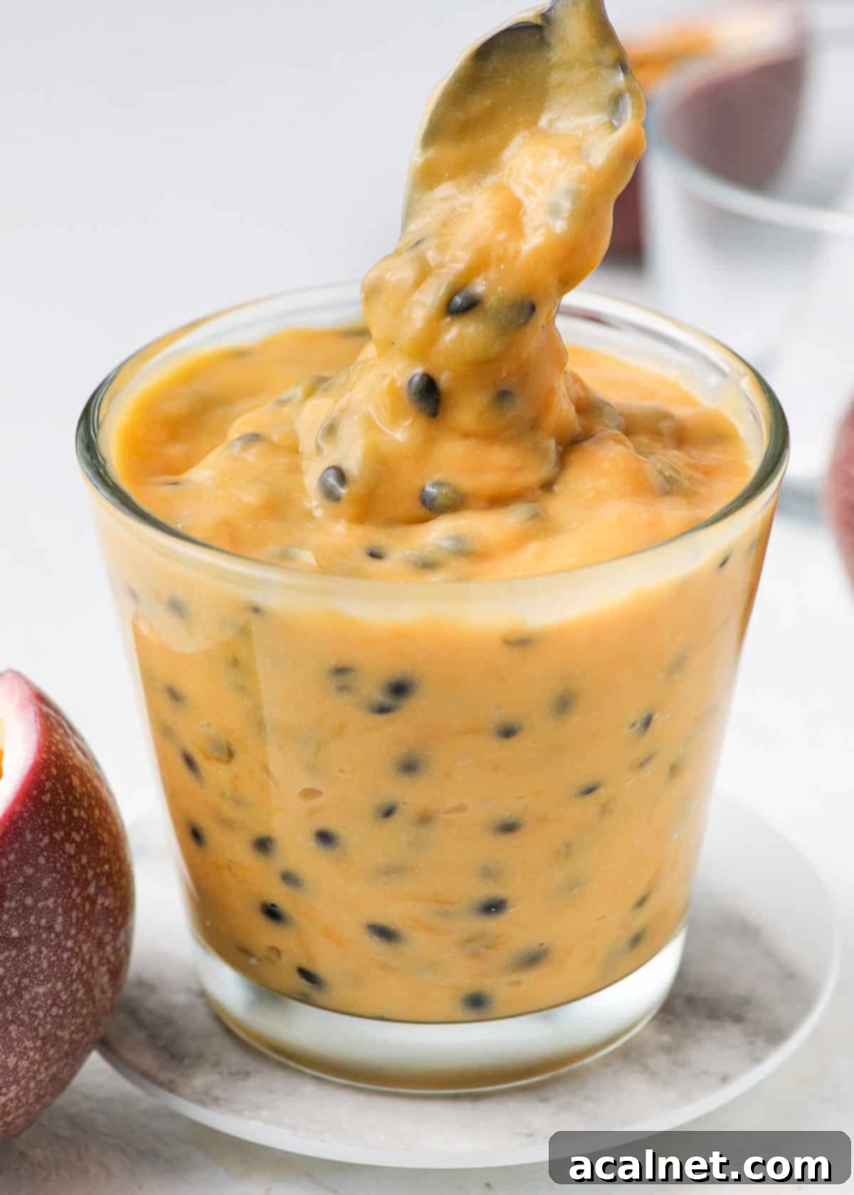 Thick, golden passion fruit curd dripping deliciously from a spoon into a small glass jar, ready for storage.