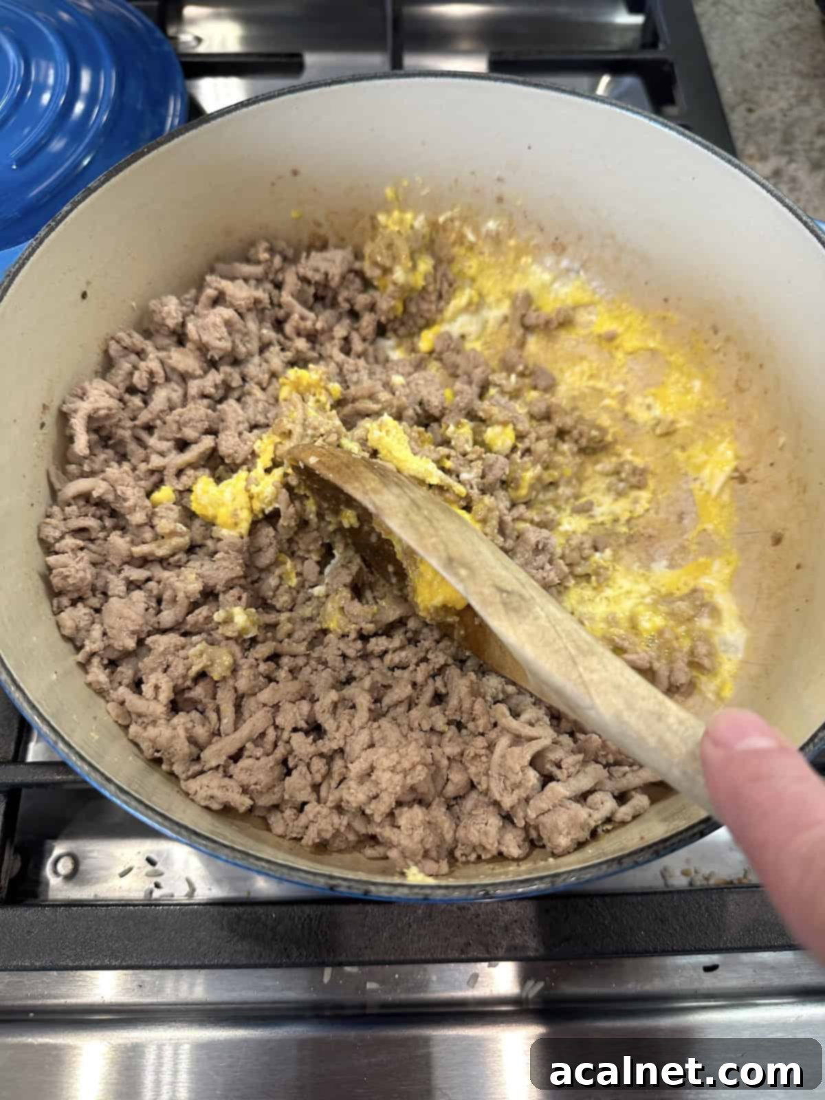 Cooked ground turkey in a pan on the stove with a partially cooked egg being scrambled on the side.