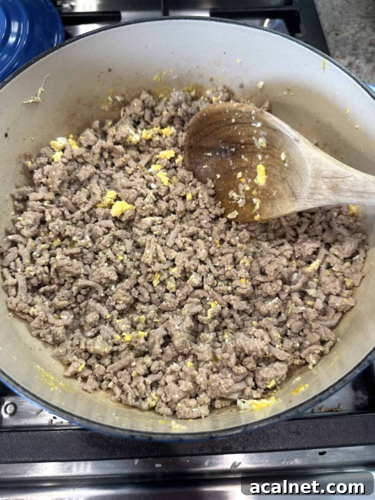 Cooked egg stirred into well-browned ground turkey in a pan on the stove.