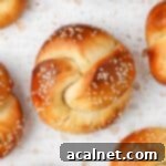 A single perfectly golden mini challah roll, topped with sesame seeds, resting on a white and pink terrazzo surface.