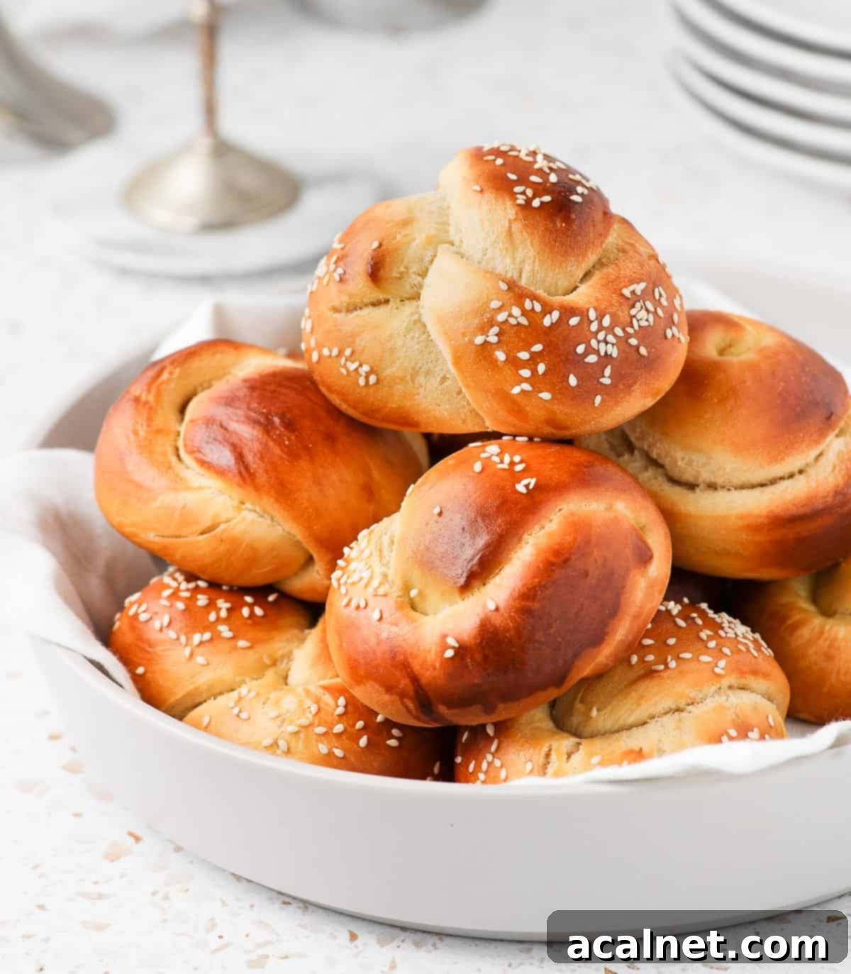 A large light grey bowl overflowing with freshly baked, golden-brown mini challah rolls, stacked high and inviting.
