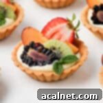 Petite Fruit & Cream Tarts 11 Close up on one mini fruit tart on a white surface, showcasing the vibrant fresh fruit topping and creamy filling.