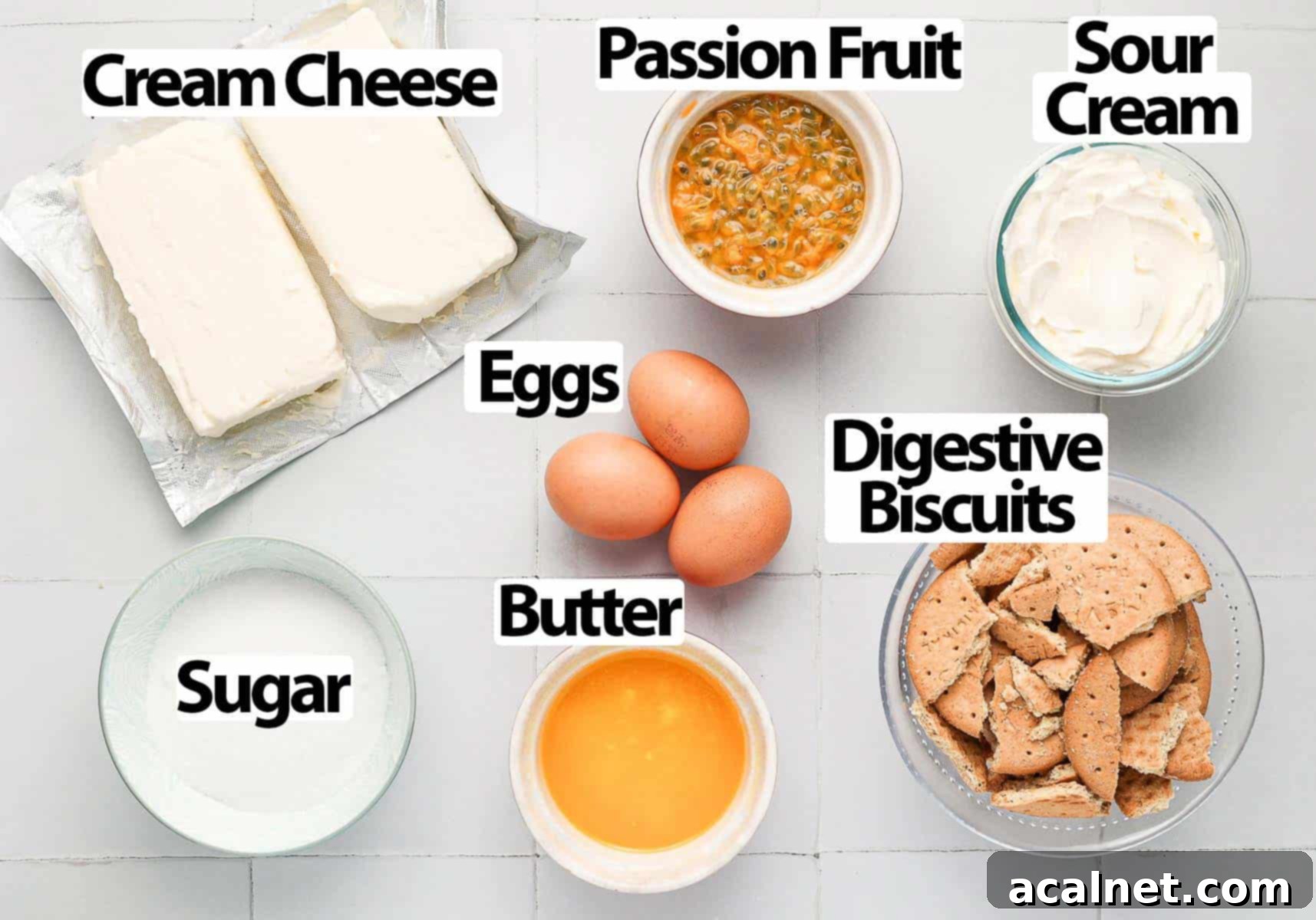 Various cheesecake ingredients laid out on a tiled kitchen surface, including cream cheese, sour cream, eggs, sugar, butter, digestive biscuits, and fresh passion fruits.