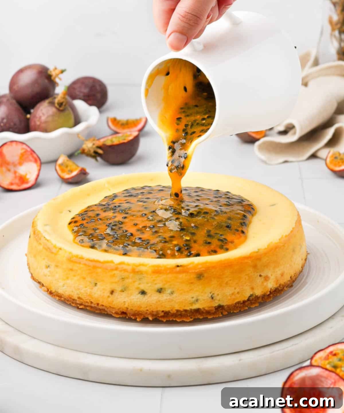 Someone pouring passion fruit coulis over the top of a creamy cheesecake, showcasing the vibrant colors and luscious texture.