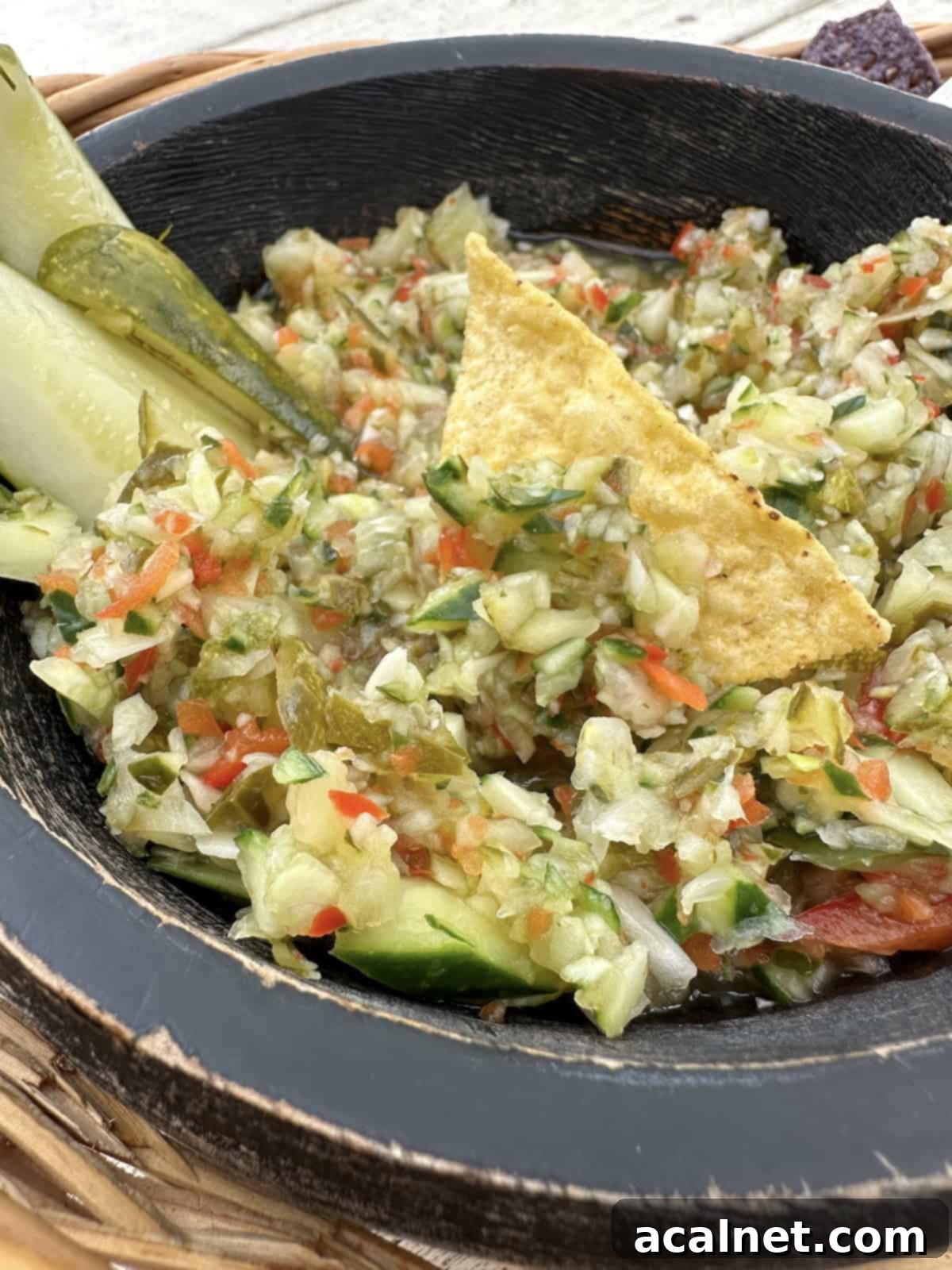 A serving bowl of pickle de gallo with pickles and a tortilla chip on top, ready for dipping.