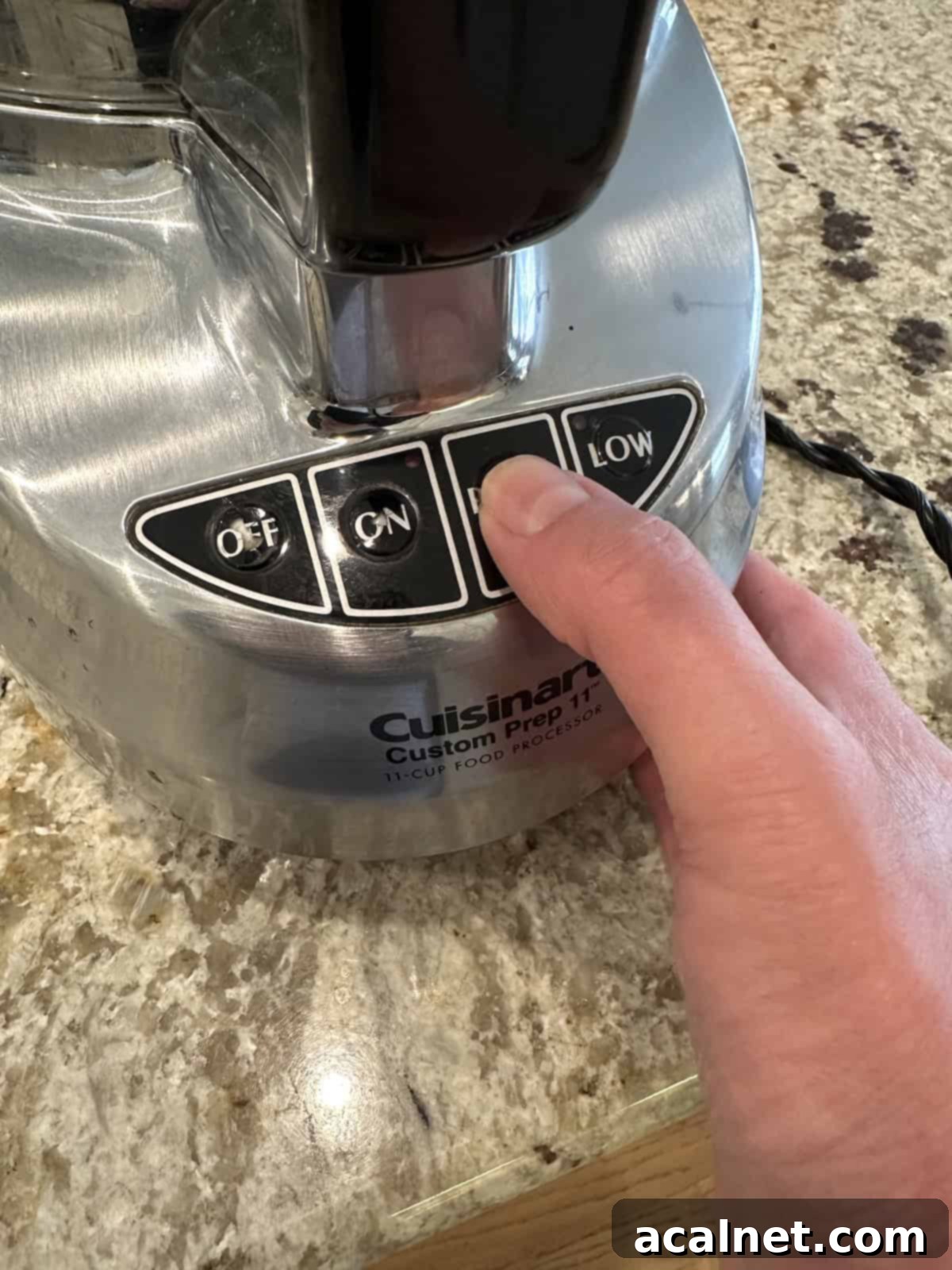 A hand resting on the base of a food processor, ready to pulse.