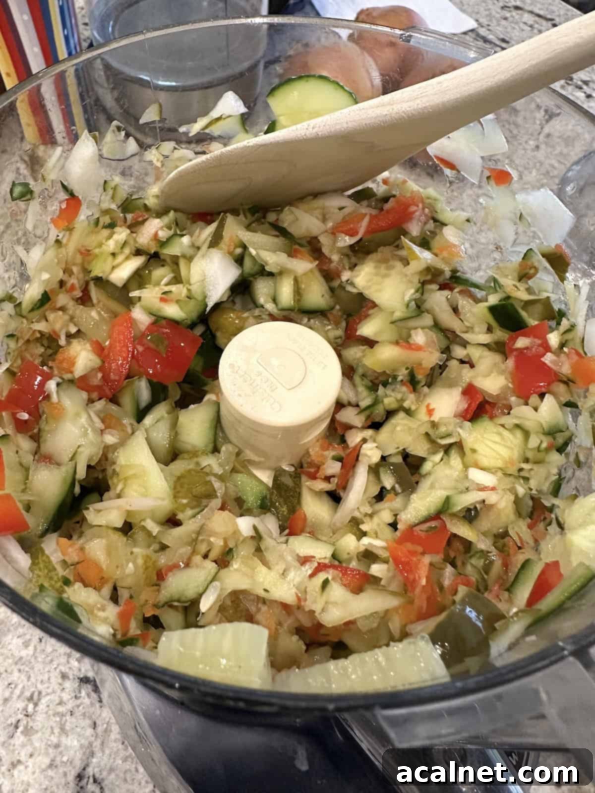 Perfectly chopped cucumbers and pickles in the bowl of a food processor, showcasing a chunky texture.