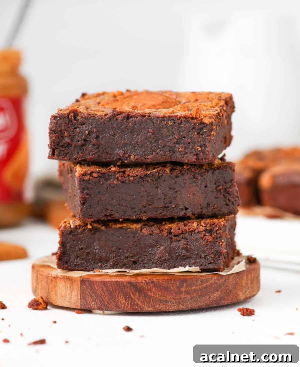 A beautifully stacked trio of dark chocolate Biscoff brownie slices resting on a small wooden coaster, showcasing their rich, fudgy interior and distinct Biscoff swirl.