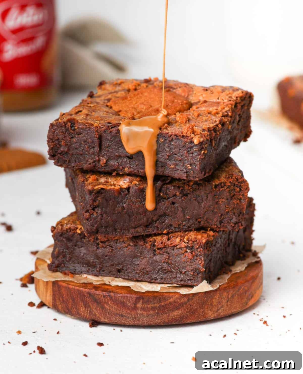 Rich Biscoff spread being generously drizzled over a stack of three fudgy dark chocolate Biscoff brownie slices, creating an irresistible cascade of flavor and visually emphasizing their decadent nature.