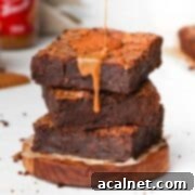 Rich Biscoff spread being generously drizzled over a stack of three fudgy dark chocolate Biscoff brownie slices, highlighting their decadent appeal.