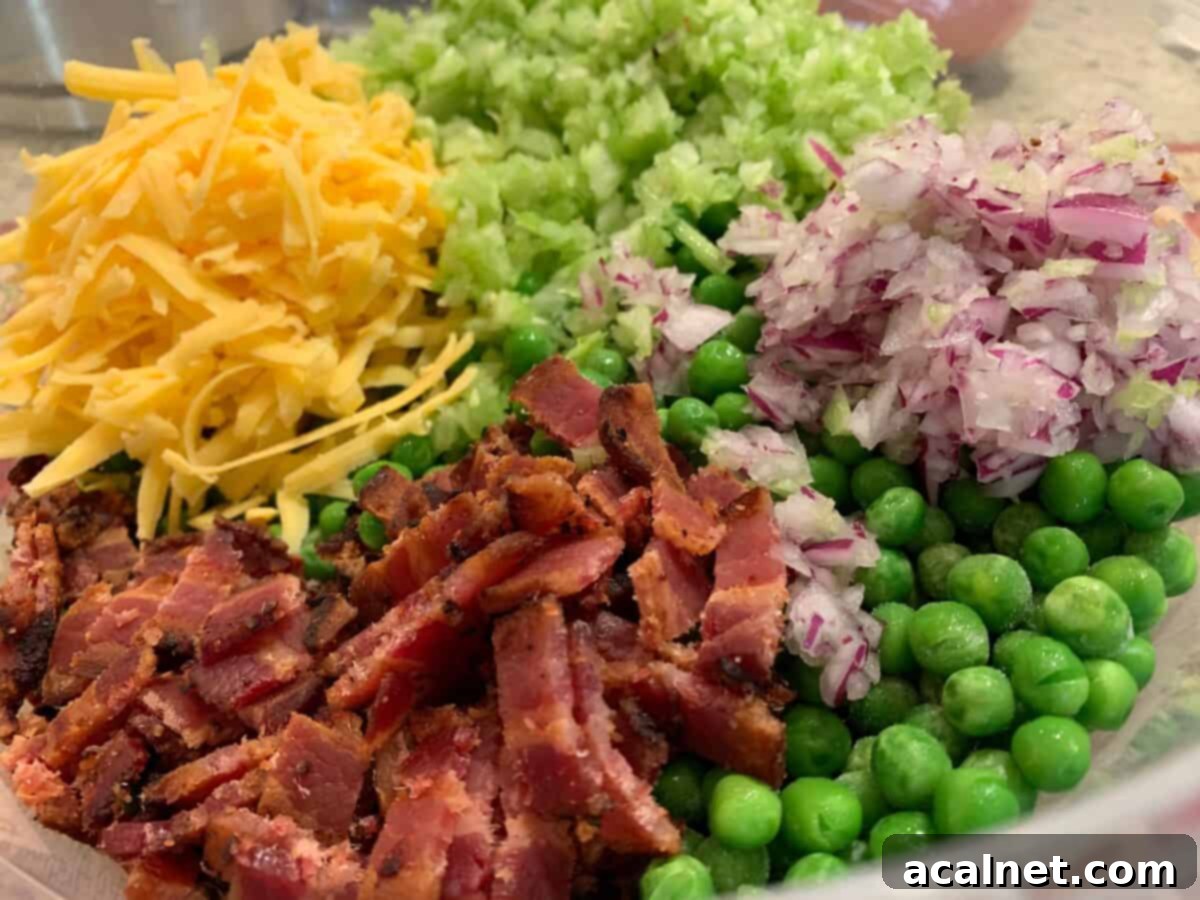 A close-up of various pea salad ingredients arranged on a wooden board: crispy bacon bits, a bowl of shredded sharp cheddar cheese, finely diced red onion, and chopped celery.