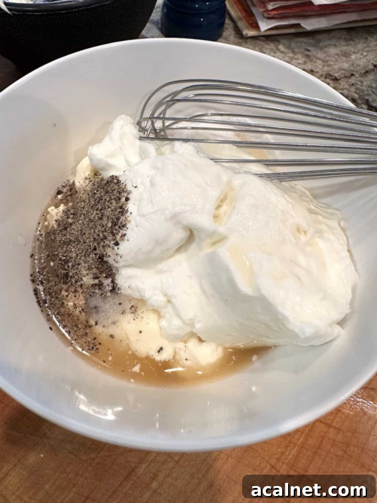 Small white bowl with Greek yogurt, mayonnaise, apple cider vinegar, and sugar, with a whisk resting in it, ready to be mixed into the dressing.