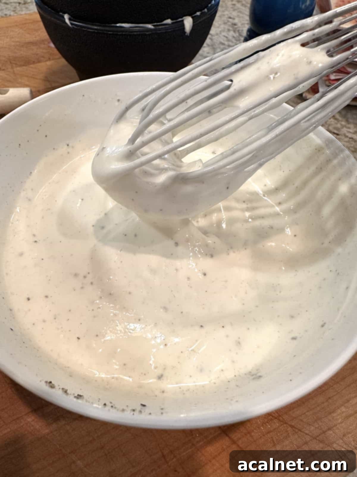 Creamy white pea salad dressing in a small white bowl, smoothly whisked with a small whisk resting inside. The texture is thick and consistent.