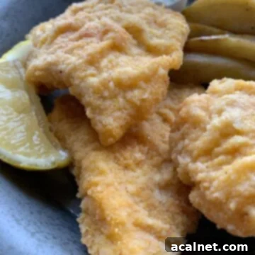Three pieces of golden fried cod on a metal plate, ready to be served with lemon.
