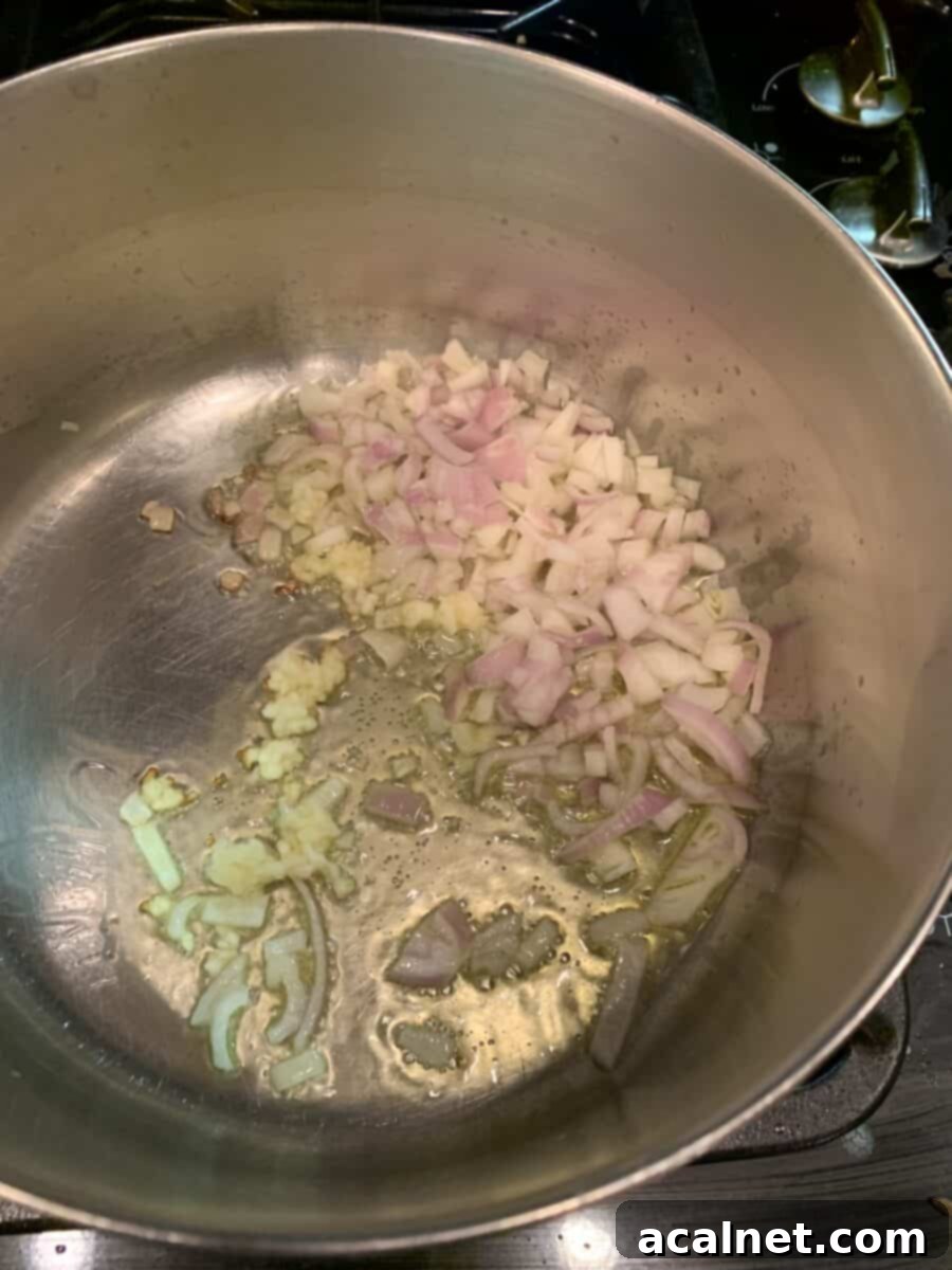 Finely diced shallots and minced garlic sizzling gently in golden olive oil in a non-stick pan on the stove, creating an aromatic base for the sauce.