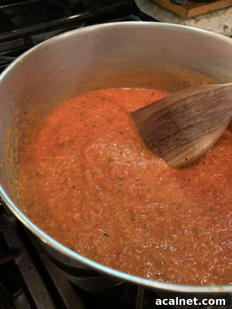 Rich and vibrant tomato-cream sauce gently simmering in a pan on the stovetop, stirred with a wooden spoon, indicating it's almost ready to serve.