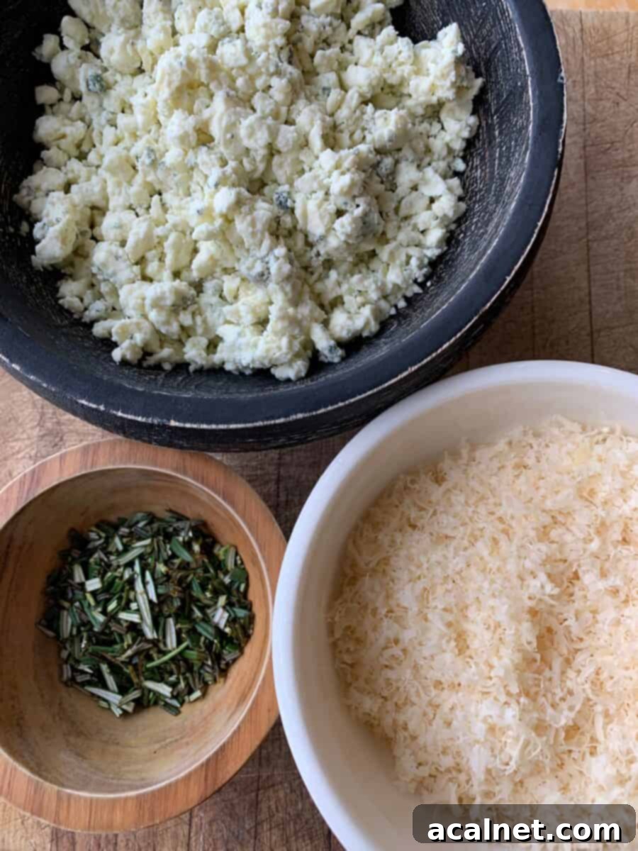 Blue cheese, parmesan and fresh rosemary in small bowls on cutting board. 