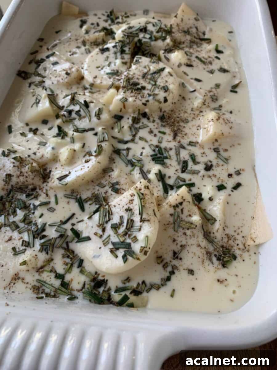 Unbaked scalloped potatoes with rosemary on top in a baking dish. 