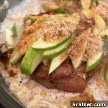 Cooked pork chops topped with sliced apples and spices in a skillet, a close-up of the delicious finished dish.