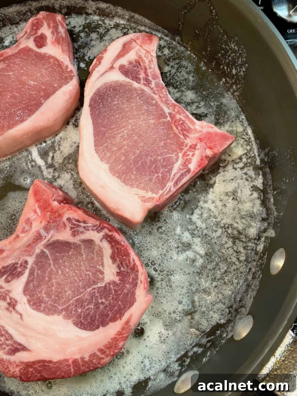 Pork chops cooking in a skillet on the stove alongside sauerkraut and apples.
