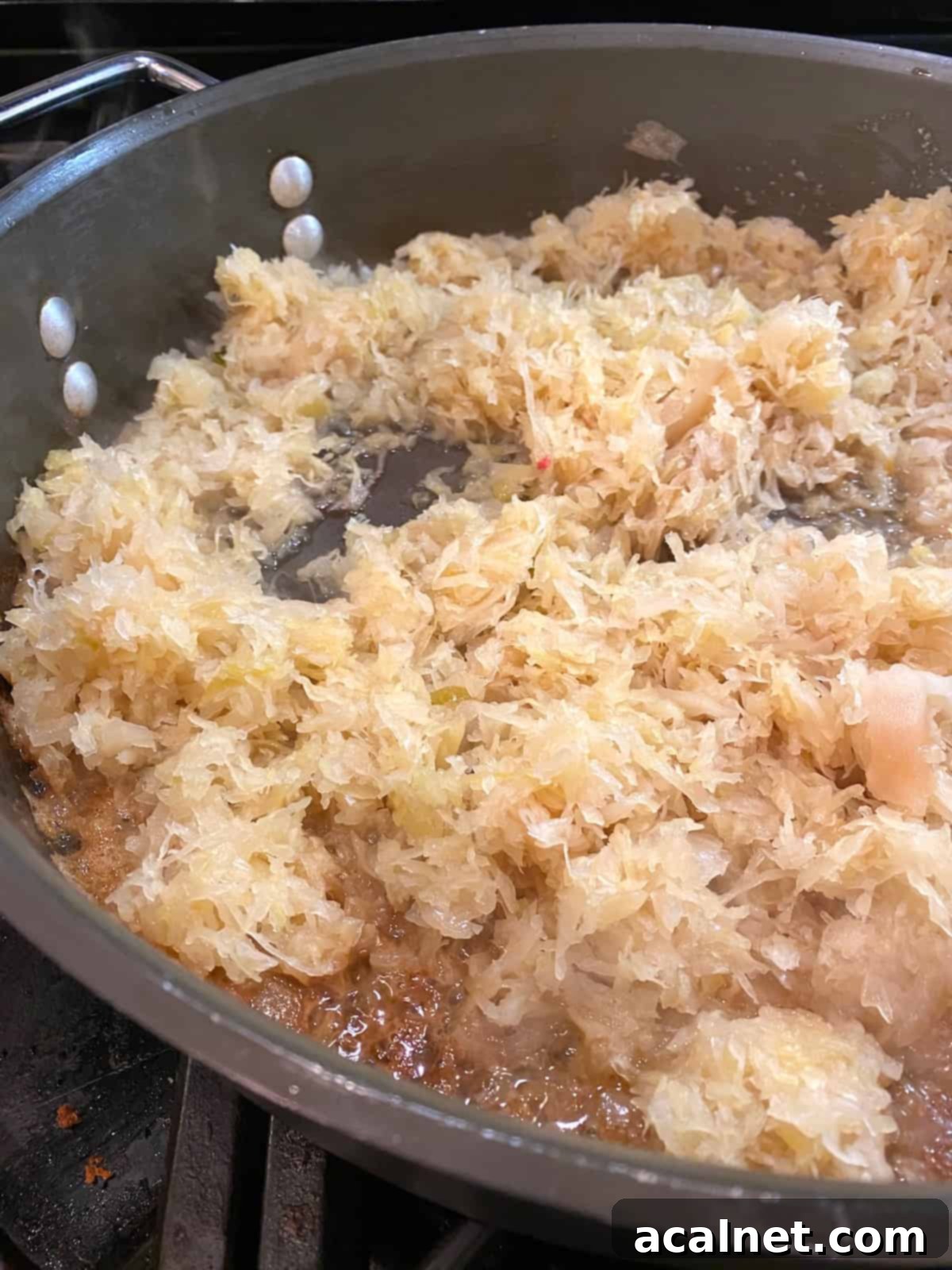 Sauerkraut cooking in melted butter in a skillet on the stove, absorbing all the delicious pork drippings.