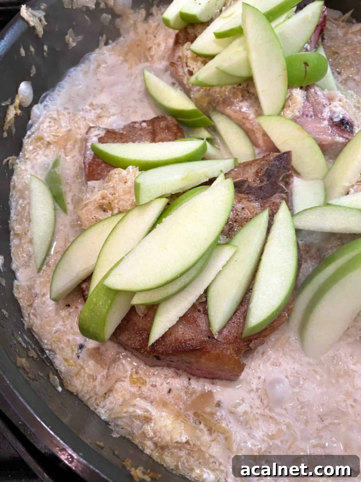 Sliced apples arranged on top of pork chops in a skillet, ready for simmering.