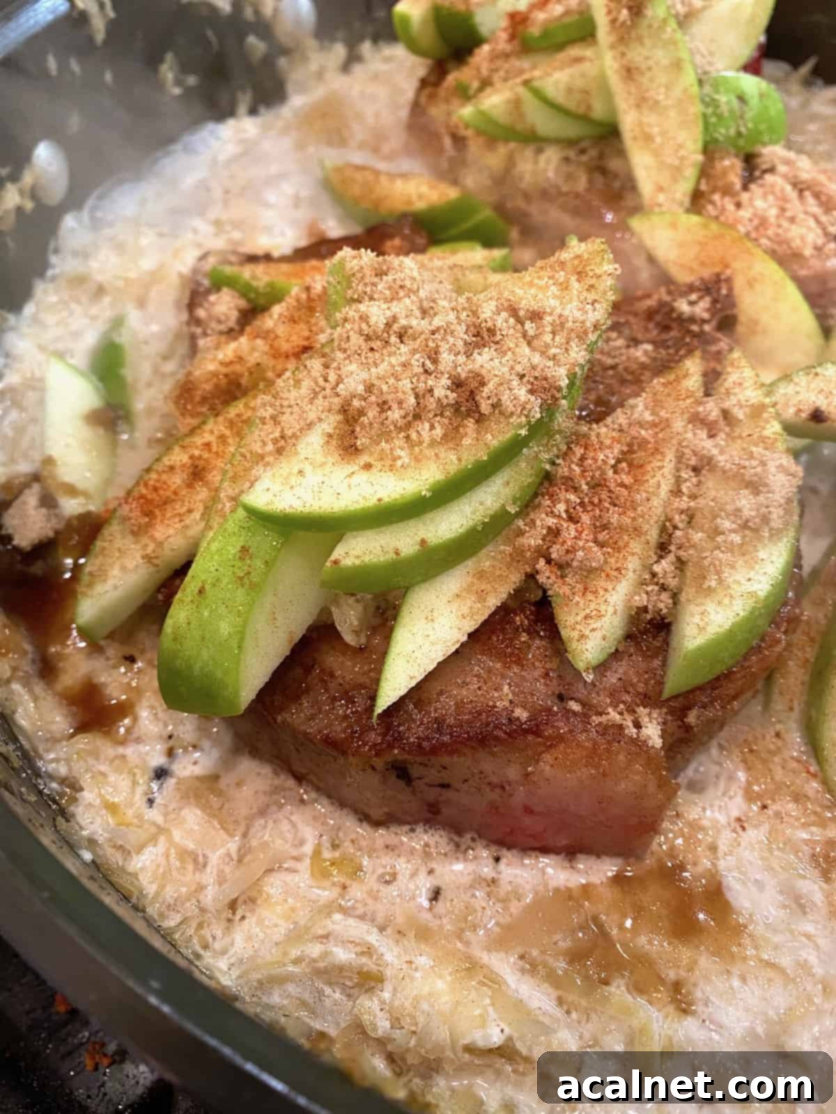 Cooked pork chops topped with tender sliced apples and a hint of spices in a skillet.
