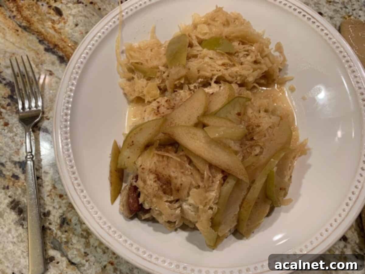 Diced, cooked apples and sauerkraut placed on top of cooked pork on a plate, ready to serve.