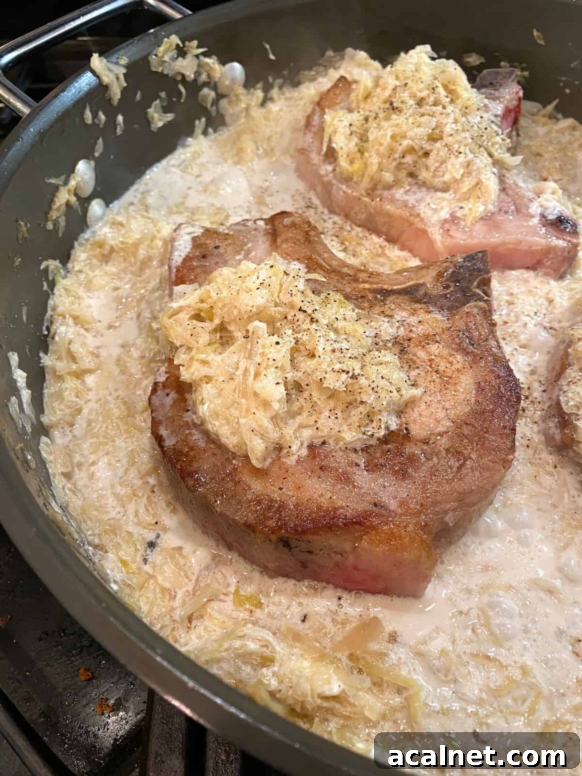 Cooked pork chops with a dollop of sauerkraut on top of each one, in a skillet, showcasing the tender result.