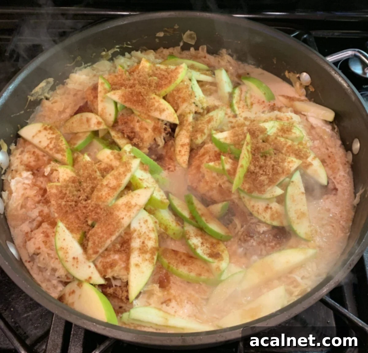 Pork chops, kraut and sliced apples in a large pan on the stove, garnished and ready to serve.